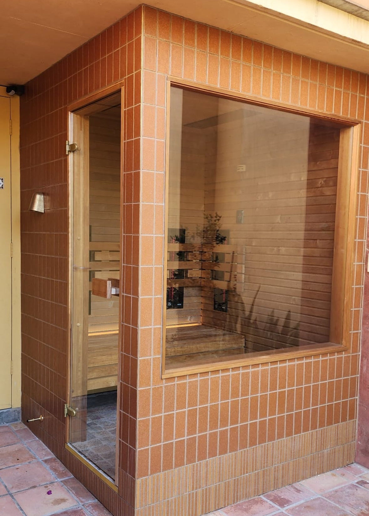 Outdoor sauna with tiled walls and floor, glass door, and wooden interior.